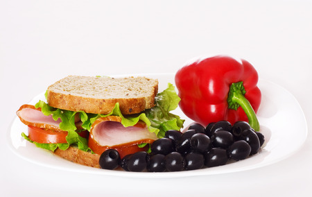 Big healthy sandwich with wholewheat bread, ham, tomatoes,  pepper, olive and curly lettuce on the plate.の写真素材