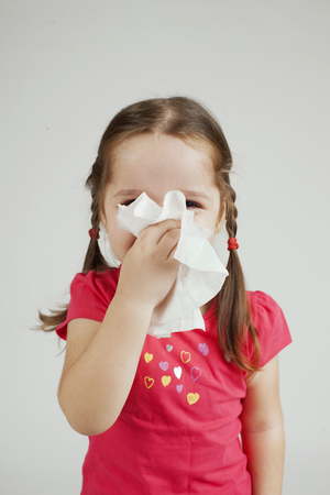 Little girl wipes her nose with a tissue.の写真素材