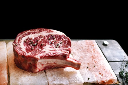 Bone In Rib Eye row Steak on pieces of salt on a wooden board. Stock imageの写真素材