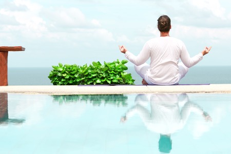 Caucasian man in white clothes meditating yoga on the sea shore pierの写真素材