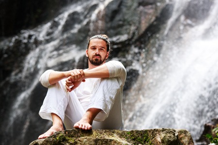 Man sitting in meditation yoga on rock at waterfall in tropicalの写真素材