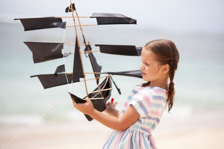 Girl playing on beach flying ship kite. Child enjoying summer.の写真素材