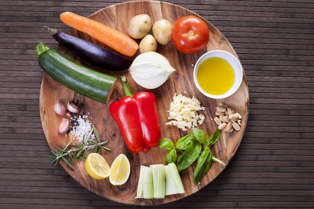 Ingredients vegetables for soup with pesto sauce and basil on a wooden plate.の写真素材