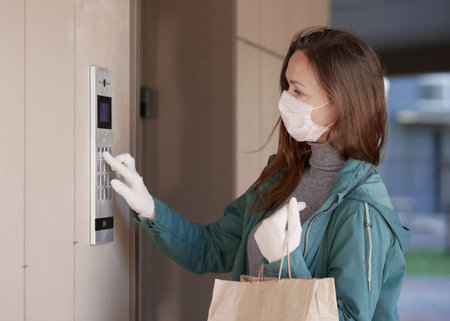 Couriers hands in black medical gloves deliver parcels in paper bag to the door during the epidemic...