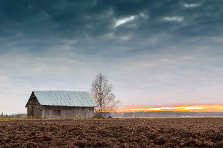 The barn house stands tall against the dramatic sky of the spring sunset. There are quite a lot of this kind of places in the Northern Finland.の写真素材