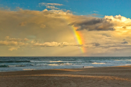 The rainbow's end seems to be on a beach at the Gold Coast City, Queensland, Australia. A lonely walker looks like she's looking for the pot of gold.の写真素材
