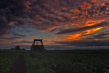 The farmer has left his tractor to wait for another day in the potato fields. The summer sun sets dramatically behind the old farming tool at the Northern Finland.の写真素材