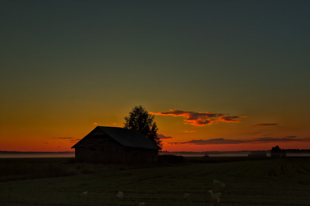 The setting sun colors the clouds golden on a summer night in the Northern Finland. The mist rises from the fields in the background.の写真素材