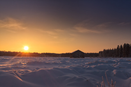 The sun rises on a cold wintertime morning in the Northern Finland. The sunlight colors the snowy field beautifully.の写真素材