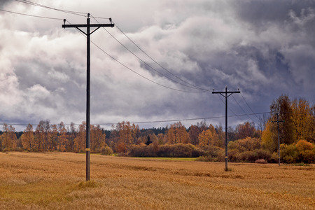 The telephone lines stand on the autumn fields under the dramatic skies in the Northern Finland. The heavy clouds predict rain showers.の写真素材