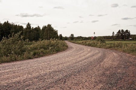 A gravel road leads by the fields to the forest in the rural Finland. There is even a speed limit for this road.の写真素材