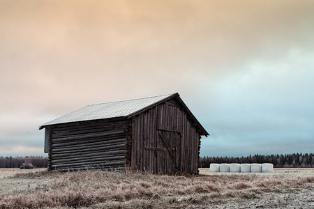 An old barn house stands on the frosty fields of the Northern Finland. The white bales are keeping the frosty barn company.の写真素材