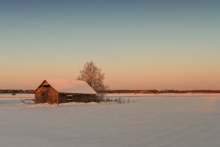The winter sun rises and colours the snow covered landscape beautifully at the rural Finland. The...