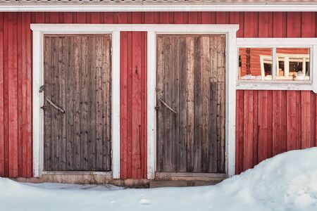 An old wooden building has two doors and a window beautifully framed with white painted wood.の写真素材