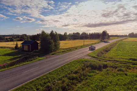 A pickup truck drives on a country road on a beautiful summer evening at the rural Finland.