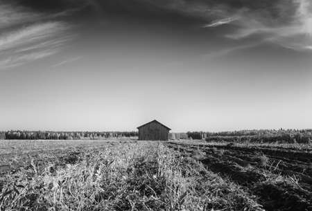 An old barn house stands a little tilted on the autumn fields of rural Finland. The harvest time is almost over.の写真素材