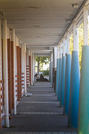 Two teenage girls are having a snack at the end of a corridor of colorful pilars on an autumn evening.の写真素材