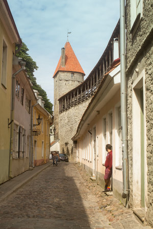 A young man is standing in the doorway at the old town of Tallinn, Estonia. He is watching the tourist girls walking by.の写真素材