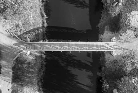 A small wooden walking bridge crossing the river. The autumn sun creates long shadows over the river water.の写真素材