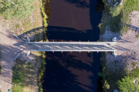 A small wooden walking bridge crossing the river. The autumn sun creates long shadows over the river water.の写真素材