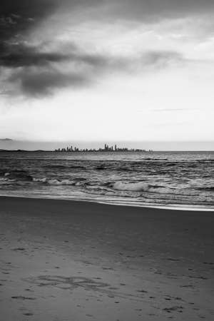 The city skyline seen from the town of Coolangatta in Queensland, Australia. Someone has drawn a flower in the sand.の写真素材