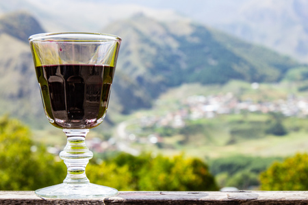 A glass of Georgian red Wine stands on a wooden railing on the background of the Georgian village...