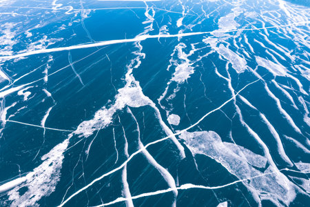 Aerial top view to Blue clear ice lake Baikal. Crack covered snow on frozen water surface. Cold...