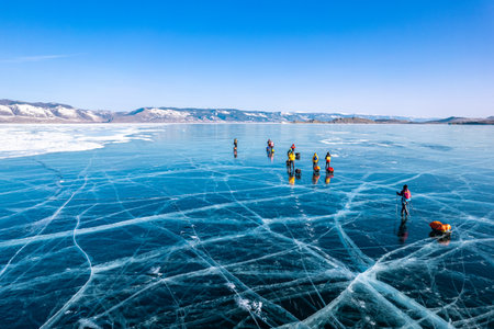Aerial top view to tourist walk go on smooth surface. People with sleds moves along the blue clear ice. Winter crossing of Lake Baikal. Cracks glossy hummocks snow. Olkhon, Small Sea, Siberia, Russiaの写真素材