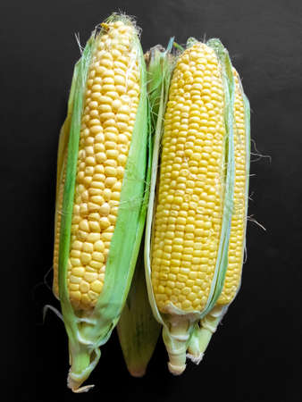 Four corns on top of each other lie flat on black.