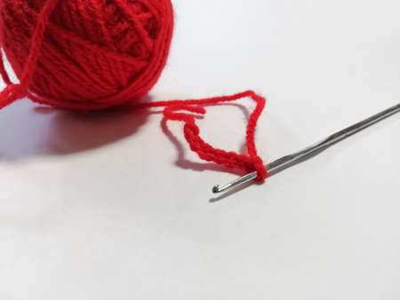 On a white background, the started crochet of red threads rolled up in a ballの写真素材