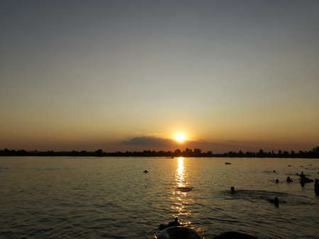 Silhouettes of people and the reflection of the sun at sunset in the water.の写真素材