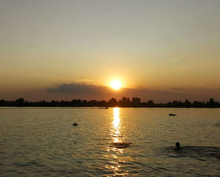 Silhouettes of people and the reflection of the sun at sunset in the water.の写真素材