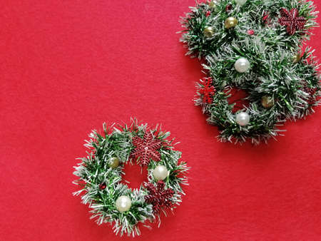 On a red background, green wreaths of tinsel and colored beads. Snowflakes.