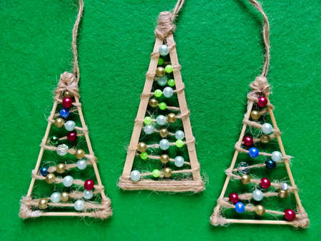 On a green background, Christmas trees with their own hands from sticks, twine and beads. Hanging decorations for new year and Christmas.の写真素材