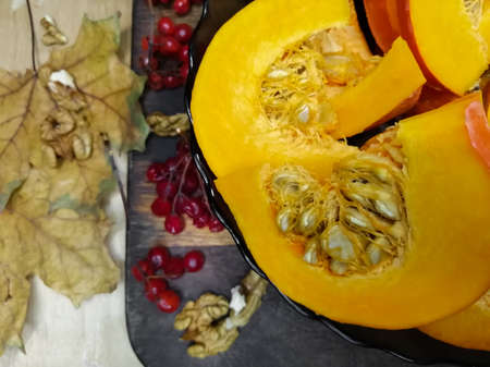 Dry leaves and viburnum on the table. Next to it in a plate is a chopped, orange pumpkin.の写真素材