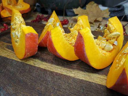 On the board are pieces of pumpkin. In the background are sprigs of viburnum, pumpkins and dry leaves.の写真素材