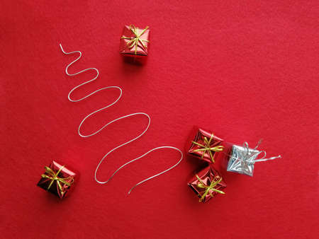 Five Christmas presents next to an artificial christmas tree made of wire on red felt.の写真素材