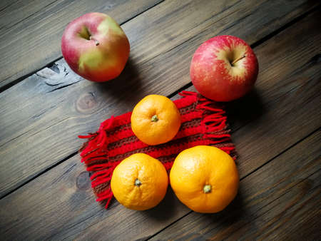 On a wooden table is a crocheted stand, tangerines and apples. Useful festive decor. Christmas and New Year's Day.の写真素材