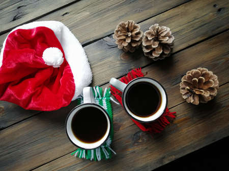 On the wooden table are the shpaks of santa, cones and two cups of hot americano. Festive coziness. Christmas and New Year.の写真素材