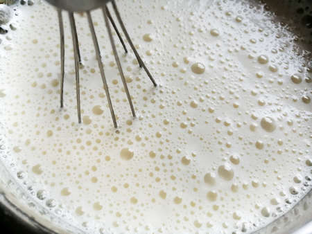 A metal whisk in a bowl with liquid dough. A lot of bubbles can be seen from above.の写真素材