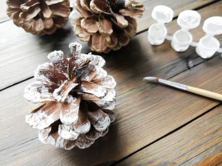 Snow-covered cones with their own hands. Homemade crafts in winter. Cones on a wooden table along with a brush and paints. Crafts with children.の写真素材