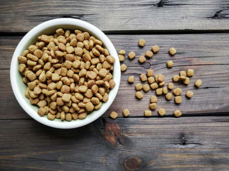 Cat food in a bowl on a wooden floor. Dry food is scattered next to the bowl.の写真素材