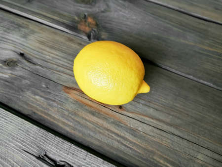 A ripe, yellow lemon lies on a wooden table.の写真素材