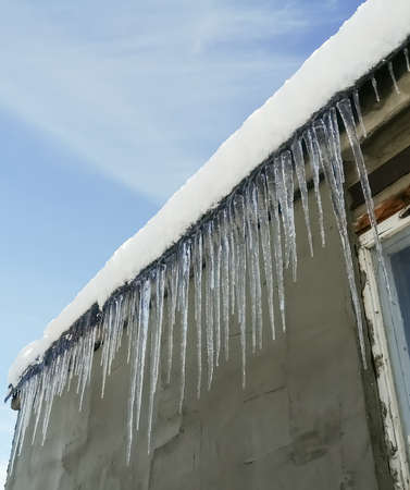 Dangerous sharp icicles hang from the roof. Beautiful icicles made of melted snow. Transparent large icicles on the edge of the roof, it is dangerous to walk.の写真素材