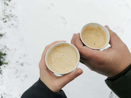 Two cups of coffee in disposable paper cups in a woman's and a man's hand. Winter. Hot coffee...