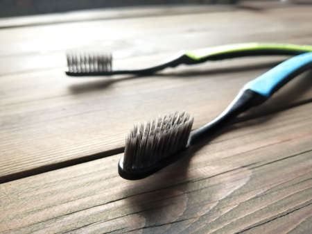 Two toothbrushes lie on a wooden table. Light falls from the front. Toothbrush with activated...