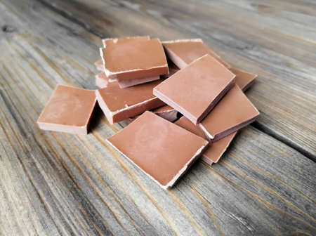 A stack of chocolate pieces on a wooden table. Milk chocolate on the table. Chocolate and wood.