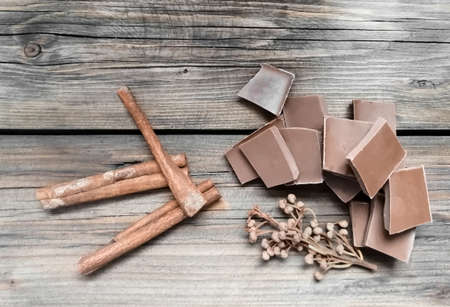 On a wooden table are pieces of chocolate, cinnamon sticks and laurel seeds. Milk chocolate with...