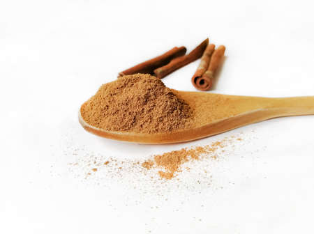 In a wooden spoon with a slide is poured powder of crushed cinnamon. Nearby are sticks of whole cinnamon. Wooden spoon with seasoning on a white background.の写真素材