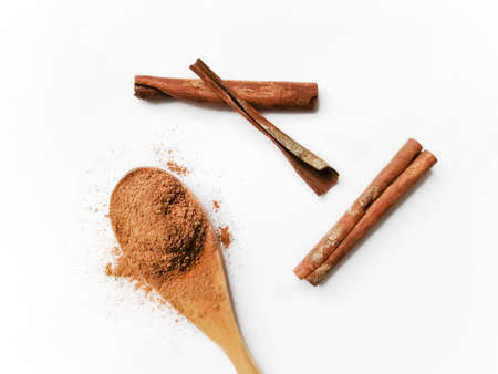 In a wooden spoon with a slide is poured powder of crushed cinnamon. Nearby are sticks of whole cinnamon. Wooden spoon with seasoning on a white background.の写真素材